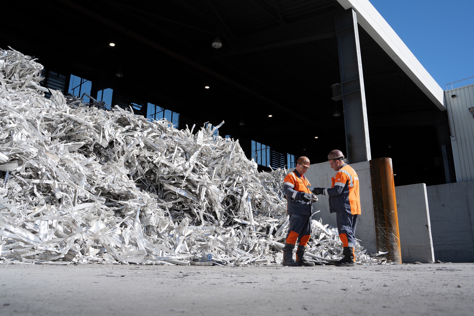 men in orange and grey overalls standing next to a pile of shredded metal